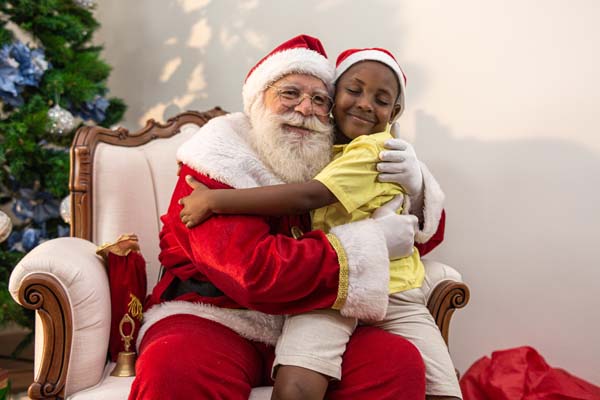 Santa Claus delivering a gift box to a little African boy. Hug.